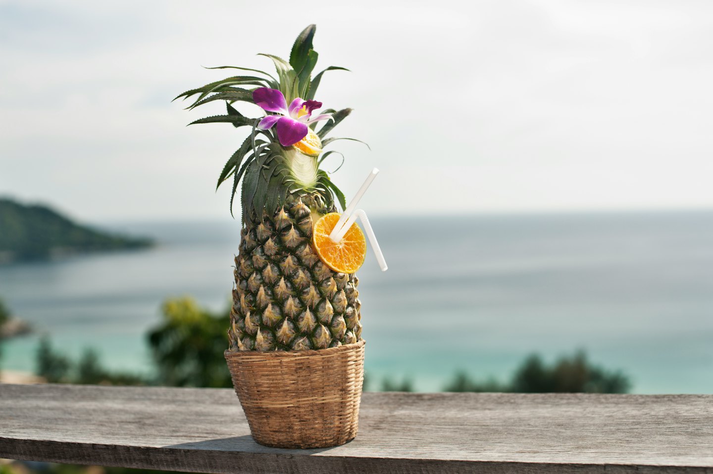 Tropical drink served in a hollowed pineapple on a wooden railing.