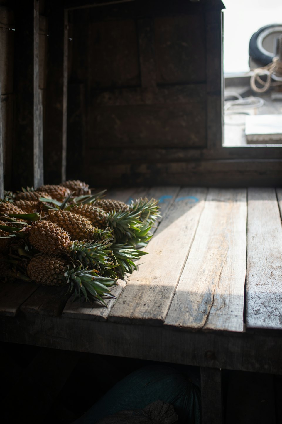 Fresh pineapples sit on weathered wooden planks at a market.